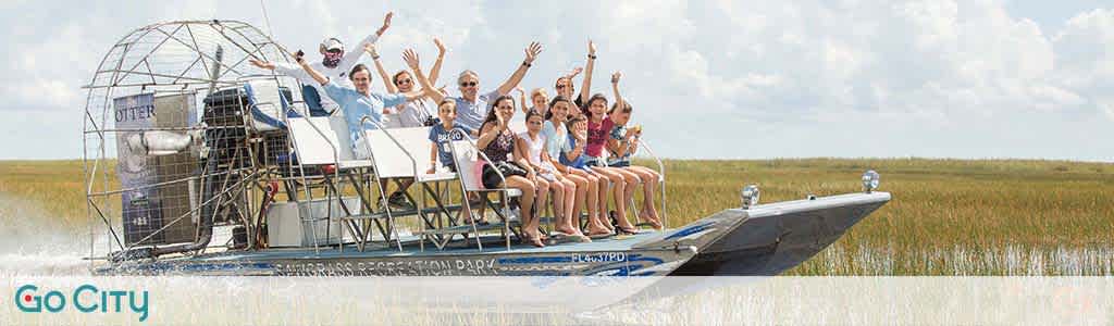 Group of excited people on an airboat tour, arms raised, with open grassland around.