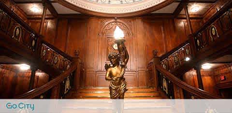 A grand wooden staircase with a statue centerpiece under arches, illuminated warmly.