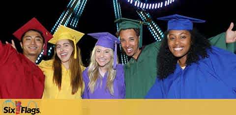 Group of five jubilant graduates in colorful robes, with caps, smiling widely, with arms raised in celebration. They stand before a blurred backdrop of an amusement park with a Ferris wheel, under the logo Six Flags. The graduates embody a spirit of achievement and fun.