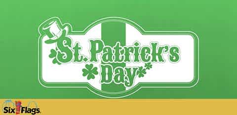 Image featuring a bright green background with a banner in a lighter green shade. The banner has an intricate border and reads 'St. Patrick's Day' in decorative white text, flanked by shamrock designs. Below the banner is a narrow golden yellow stripe. In the bottom left corner is the Six Flags logo.