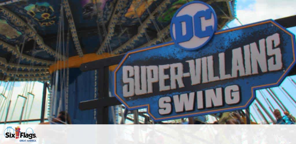 Image shows a theme park ride sign reading 'SUPER-VILLAINS SWING' with the DC logo, set against a blurred backdrop of a swinging carousel and bright blue sky, indicating an attraction inspired by DC comics characters at a Six Flags amusement park.