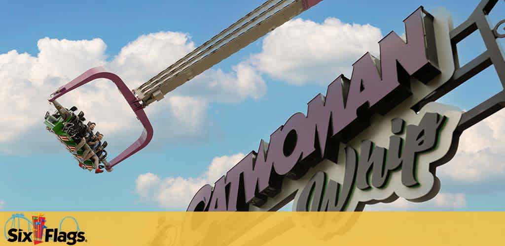 Image shows a thrill ride at Six Flags amusement park called Catwoman Whip. A carriage with excited riders is swung horizontally high in the air against a backdrop of blue skies with clouds. The ride's sign displays the attraction's name in stylized letters with the iconic Six Flags logo below.