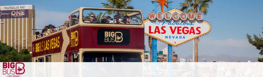 Image showing a red, open-top, double-decker sightseeing bus labeled 'Big Bus Las Vegas' in the foreground. Passengers are visible on the top deck enjoying the view. In the background, the iconic 'Welcome to Fabulous Las Vegas Nevada' sign is prominently displayed under a clear blue sky.