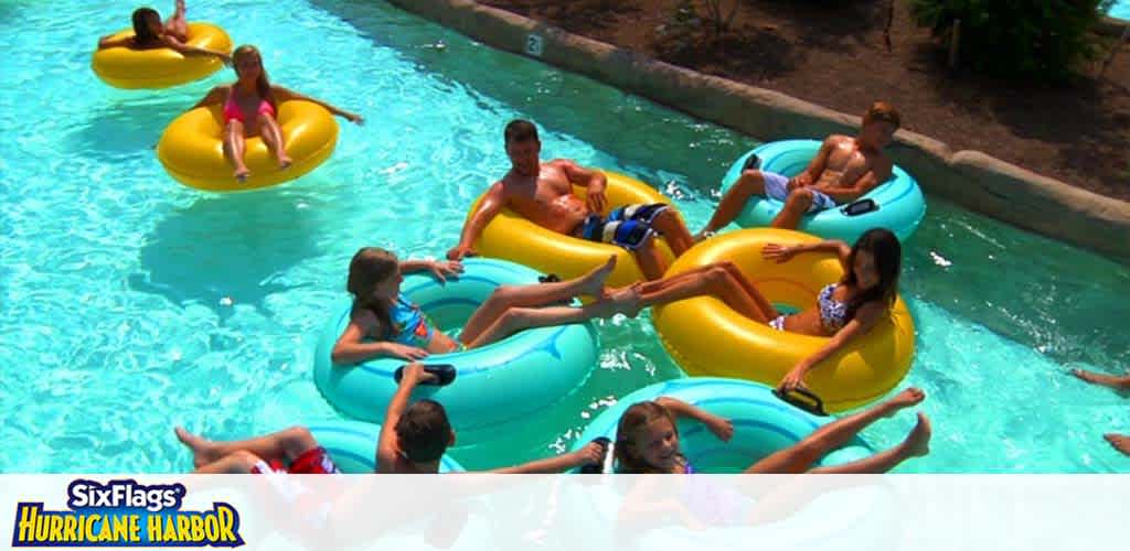 Guests enjoy floating on a lazy river in colorful yellow and blue tubes at Six Flags Hurricane Harbor. The water is clear and there’s greenery alongside the river’s edges. The sunny day adds to the relaxed, fun atmosphere.