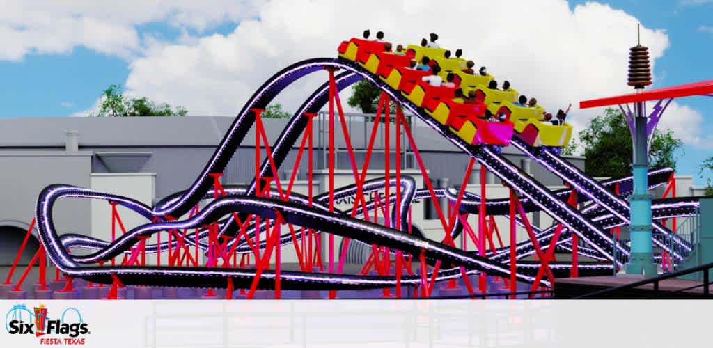 Image displays a colorful roller coaster with blue tracks and red supports at a Six Flags theme park. A filled coaster train is seen cresting a hill, with excited riders raising their hands. The background features a clear sky and park buildings. The Six Flags Fiesta Texas logo is visible at the bottom.