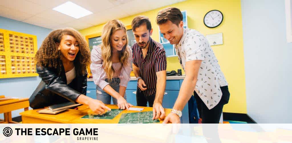 Four people collaborate enthusiastically around a table in an escape room, pointing at clues. They're in a brightly lit room with colorful walls, lockers in the background, and an air of excitement. The photo includes a watermark for The Escape Game Grapevine.