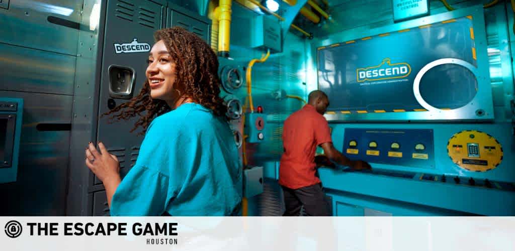 A woman and a man engage in a playful escape game. She looks on with a delighted smile, while he works on a puzzle at a themed console labeled DESCEND. They're surrounded by vibrant turquoise walls and mock equipment, creating an immersive submarine environment. The logo of The Escape Game Houston is visible.