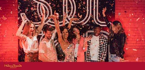 A group of six joyful people are dancing in front of a neon sign that reads SOUL on a brick wall. They're in a dimly lit room with a festive atmosphere, highlighted by sparkling confetti in the air. Their expressions and raised hands suggest they are having a great time.