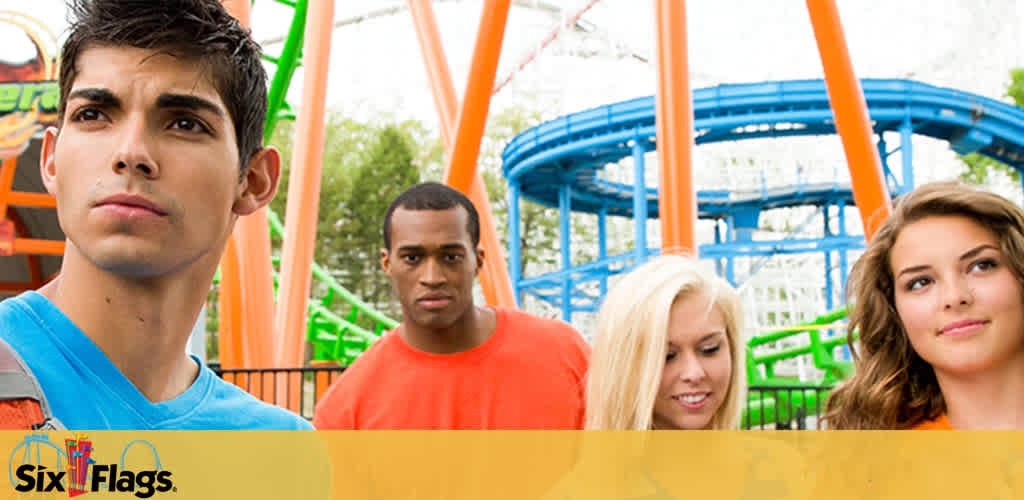 Image shows a group of four young adults with a theme park background featuring roller coasters. Two males and two females in casual attire with varying expressions of anticipation and excitement. The Six Flags logo is visible at the bottom.