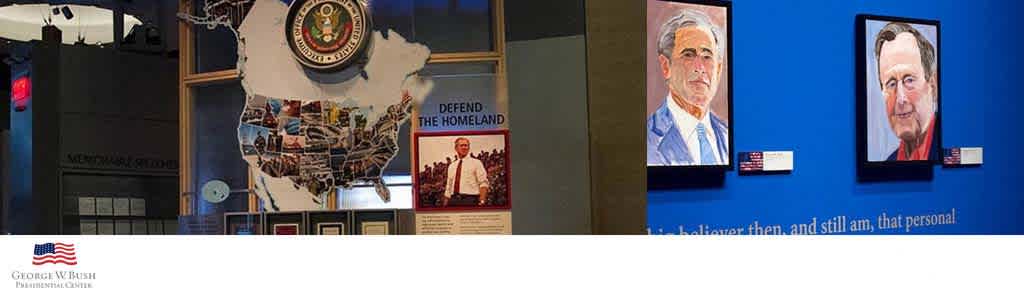 The image shows an interior view of a gallery with various exhibits. On the left, a large cut-out graphic of the United States adorned with multiple images is displayed above a section labeled 'Defend the Homeland.' To the right, two portraits of men are hung on a navy blue wall. Below the portraits, informational plaques provide details about the displayed items. The logo of the George W. Bush Presidential Center is visible at the bottom, indicating the location. The environment suggests an educational and historical context