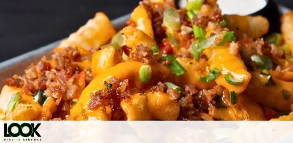 A plate of cheesy fries topped with bacon bits and green onions.