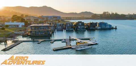 This image features an aerial view of Aero Adventures, a water-based adventure facility during the golden hour, with the sun setting in the background. The facility consists of several floating structures on calm waters, including a dock and buildings that likely serve as both operational hubs and guest areas. A seaplane is docked alongside one of the pontoons, ready for an aquatic takeoff or just arrived from an aerial excursion. Clear skies and the gentle radiance of the setting sun provide a serene and inviting atmosphere. Surrounding the facility, a serene body of water is visible, with distant rolling hills forming a picturesque backdrop.

At FunEx.com, we're committed to bringing you the lowest prices and exclusive savings on tickets for incredible experiences, and Aero Adventures is no exception. Discover your next adventure with us and take advantage of our amazing discounts!