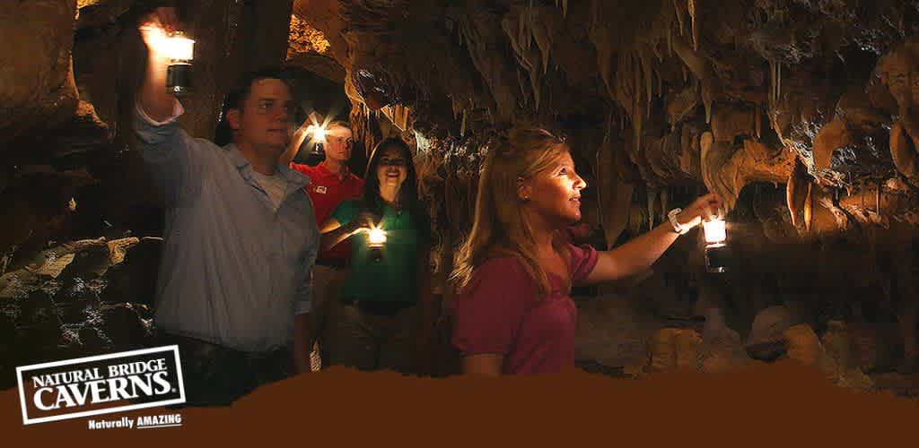 Group of people on a cave tour holding lanterns. A woman in the foreground gestures excitedly, highlighting stalactites above, while others look on. The cavern's rocky textures are illuminated warmly by the lantern light.  Natural Bridge Caverns - Naturally AMAZING  is inscribed below.