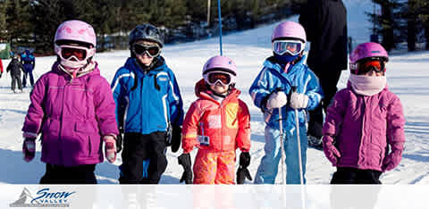 Image Description: The image features a group of five children standing on snow, prepared for a day of winter sports. From left to right, the first child wears a vibrant pink ski jacket and a pink helmet with matching goggles. Next to them stands a child in a blue ski jacket and dark pants, also wearing a helmet and goggles. The middle child is dressed in a bright orange snowsuit, with a small stature indicating they are the youngest in the group. This child has a blue helmet and goggles. To their right, another child is outfitted in a blue ski jacket and helmet with a lighter blue tint on the goggles. The final child on the far right wears a purple jacket, and like the others, is equipped with a helmet and goggles. They are all holding ski poles and appear ready to enjoy the snow-covered slopes in the background, under a clear blue sky. The snow beneath their feet is well-trodden, suggesting a popular ski area. A logo in the bottom left corner reads 'Snow Valley.'

End with discount-related sentence: Plan your snowy adventure now and enjoy savings on lift tickets with the lowest prices of the season, only at FunEx.com.