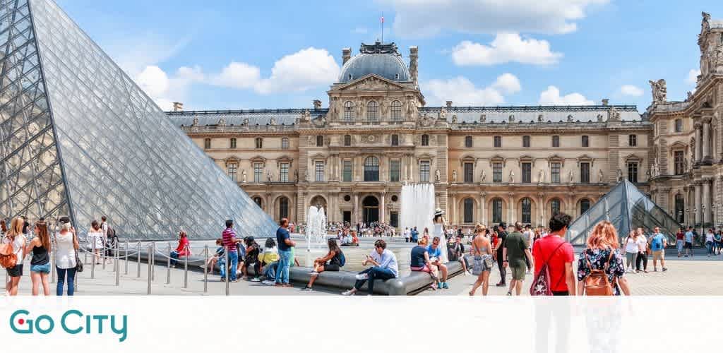 Image shows visitors at a famous landmark with a large glass pyramid and a historic palace in the background. People are sitting and walking around the courtyard on a sunny day. The sky is blue with some clouds, and the Go City logo is at the bottom.