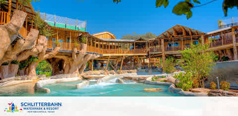 Image displays a sunny day at Schlitterbahn Waterpark and Resort. A clear lazy river snakes in the foreground, flanked by rock formations and lush greenery. Behind, rustic wooden structures with multiple levels suggest various water attractions. The sky is a bright blue, complementing the inviting ambiance of the park.
