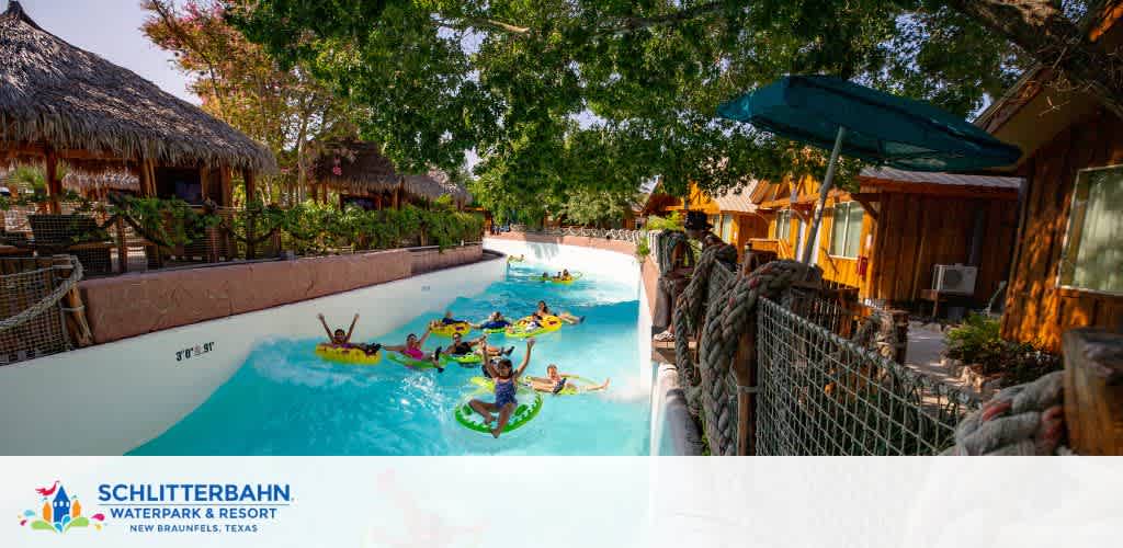 Image shows a lazy river ride at Schlitterbahn Waterpark & Resort in New Braunfels, Texas. People in colorful swimwear are floating on inner tubes, with tropical-style thatched huts and greenery alongside the water course. The sky is clear and suggests a sunny day.