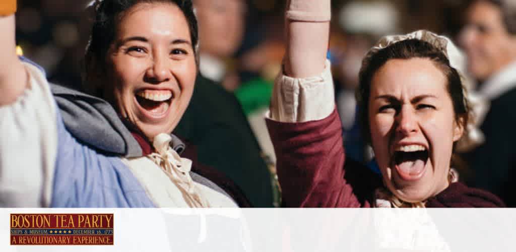 The image features two enthusiastic women dressed in historical attire, celebrating at a Boston Tea Party reenactment event. They are smiling and cheering with one woman's fist triumphantly raised. The background is blurred, focusing on their expressions of joy. Text overlay promotes the Boston Tea Party Ships & Museum as a revolutionary experience.