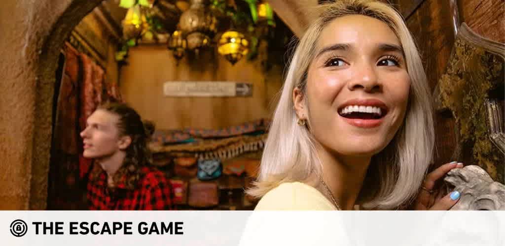 Image description: A vibrant and exciting escape room adventure is captured in this image. In the foreground, a young woman with a wide, joyful smile appears to be the picture of excitement. She has shoulder-length blonde hair and displays a look of elation with her eyes looking slightly upwards. Her attire suggests a casual outing, and her fingernails are painted with a light blue polish. In the background, a young man in a red and black checked shirt is also part of the experience, attentively looking to his side, possibly solving a clue or deeply engaged in the game. They are both in a dimly lit room rich with ornate decor and an archway that hints at the immersive environment of the escape room. The setting suggests an atmosphere of mystery and exploration with rustic and exotic motifs.

Enhance your next adventure with FunEx.com and discover savings on tickets, experiencing the thrill of escape games at the lowest prices available.