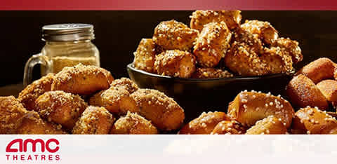 This image features a mouth-watering display of cinema snacks associated with AMC Theatres. In the foreground, there is a large, black circular plate piled high with golden-brown pretzel nuggets generously coated in salt crystals. To the left, there's a mason jar, and though its contents are not clearly visible, it suggests a casual, homey presentation. The AMC Theatres logo is prominently displayed in the lower left corner of the image, signifying brand affiliation. The backdrop is a muted red tone that complements the warm colors of the snacks. These delectable treats are indicative of the movie-going experience. At GreatWorkPerks.com, we're committed to providing the lowest prices on tickets, ensuring that your entertainment comes with great savings.