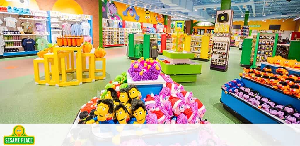 Brightly colored Sesame Place gift shop featuring shelves and bins full of plush toys, apparel, and souvenirs. Vivid greens, yellows, and blues decorate the space, with playful designs and structures throughout the store to evoke a fun, kid-friendly atmosphere.