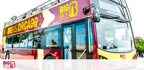 An angled view of a vibrant yellow and red Big Bus Chicago tour bus against a clear sky. The double-decker bus has an open-top deck and large side windows, with branding and the hop-on hop-off sign visible.