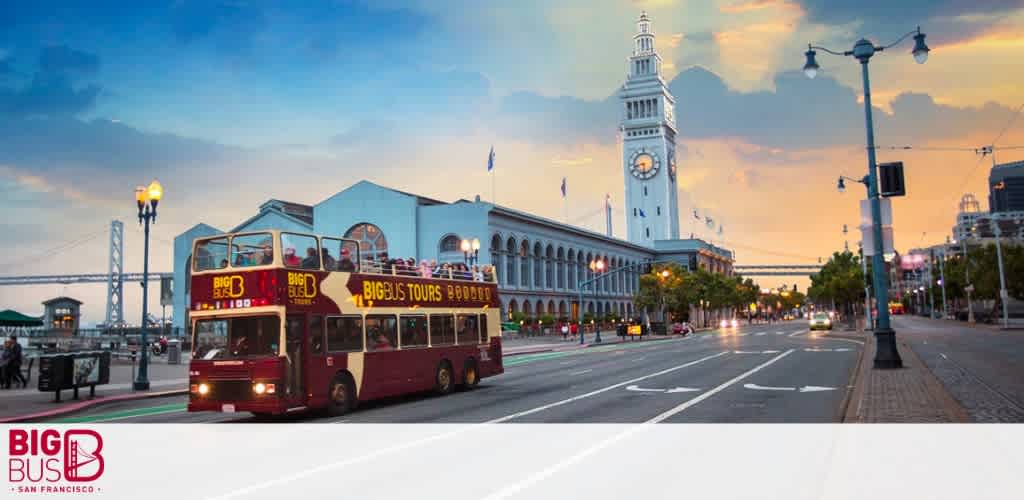 A red tour bus drives past the Ferry Building in San Francisco at dusk.