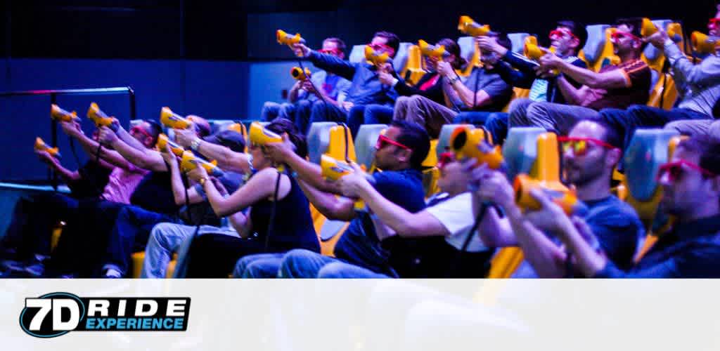 Image Description:
This image shows an exciting scene at a 7D Ride Experience attraction. A group of people, visibly immersed in the thrill of the ride, are seated in motion chairs that appear to be synchronously moving with the on-screen action. They are each holding a bright yellow gun-shaped controller, aiming towards what is presumably a screen not visible in the image. The attendees wear 3D glasses, enhancing their visual experience, and are variously expressing enjoyment and concentration. Some are leaning to one side, indicating the dynamic nature of the ride which simulates an environment that engages multiple senses. Overhead and ambient lighting provides a dim, theatrical atmosphere that focuses the attention on the shared experience. The "7D Ride Experience" logo is prominently displayed in the bottom left corner of the image, signifying the brand of the attraction.

Random Sentence:
Don't miss out on the ultimate entertainment – find the lowest prices on tickets and enjoy additional savings for your next 7D Ride Experience at FunEx.com.