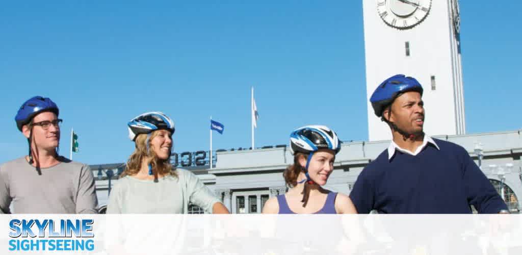 Image displays four individuals in casual attire wearing safety helmets, likely preparing for a bike tour with Skyline Sightseeing. They appear cheerful, enjoying a sunny day. In the background, a large clock tower looms under a clear blue sky, signifying a notable landmark. The company logo is in the top left corner.