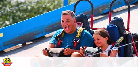 An adult and child enjoying a ride in a go-kart, both smiling excitedly.