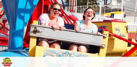 Two people laughing on a colorful amusement park ride under a bright sky.