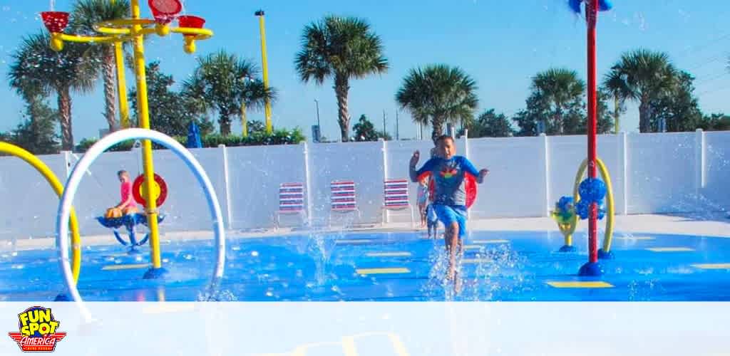 Children play in a splash pad area with colorful water features.