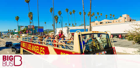 Open-top red tour bus with passengers under clear blue sky, palm trees, and signage 'Big Bus Los Angeles'.