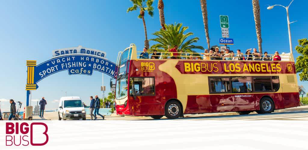 A red double-decker tour bus labeled "Big Bus Los Angeles" by the Santa Monica pier sign.