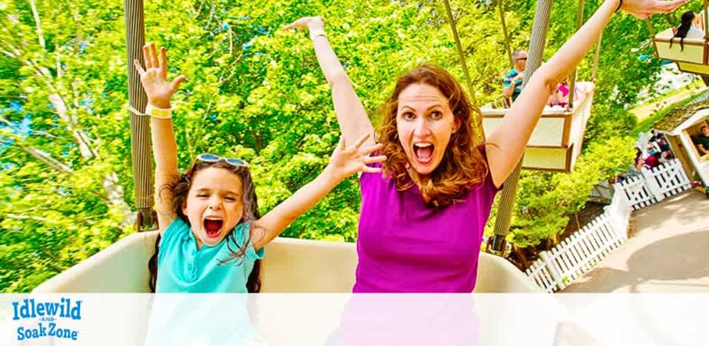 Image features a young girl and a woman with raised arms, expressions of delight, on a swing ride at Idlewild SoakZone. Trees and park visitors in the background suggest a vibrant amusement park setting. Bright sunny day enhances the joyous atmosphere.