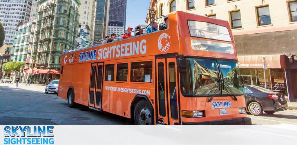 This image displays a vibrant orange double-decker tour bus prominently featuring the text "SKYLINE SIGHTSEEING" across its side and front. The bus, with its top deck open to the elements, provides an unobstructed view of the city for passengers, some of whom can be seen seated up top enjoying the tour. The backdrop showcases an urban street lined with buildings, including a notably distinctive green cylindrical structure with multiple windows, contributing to the metropolitan atmosphere. Clear blue skies above suggest a pleasant day for outdoor activities. With FunEx.com, you can explore the city's sights at your leisure and enjoy exclusive discounts and the lowest prices on tickets.