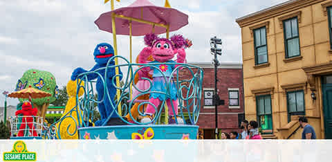 Sesame Place parade with characters on a float under a sunny sky.