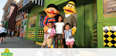 Three kids with Sesame Street characters at a theme park.