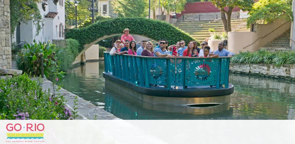 A group of tourists enjoys a boat cruise along a serene river surrounded by lush greenery and quaint architecture. The boat features vibrant blue railings with decorative patterns. A clear sky and the peaceful outdoor setting add to the leisurely experience. The GO RIO logo is visible, suggesting the cruise service.