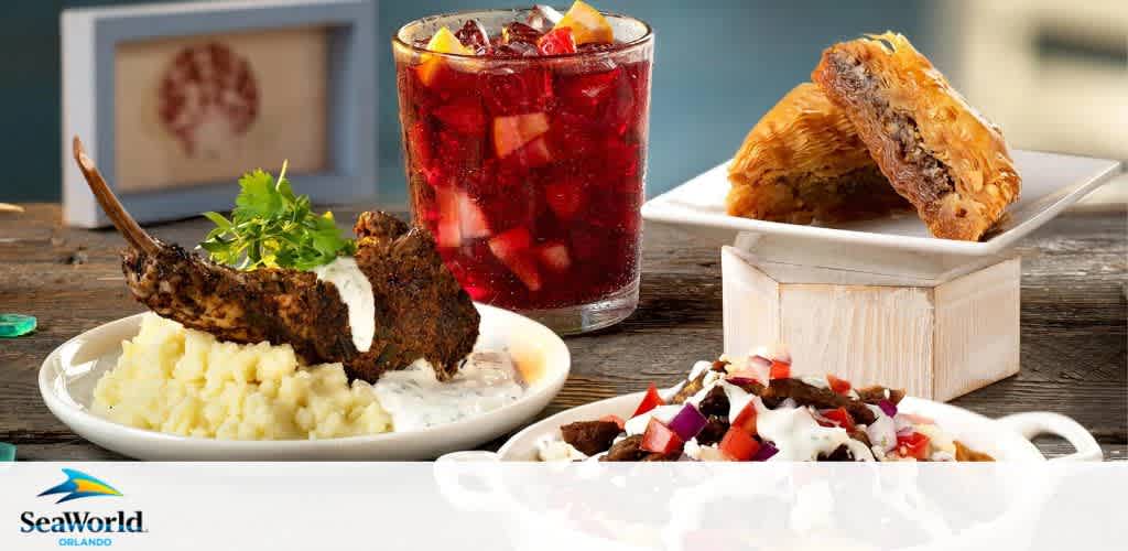 This image features a variety of dishes on a wooden surface, showcasing SeaWorld Orlando's culinary offerings. On the left, there's a plate with a seasoned lamb chop on a bed of mashed potatoes with sauce and garnish. In the center, a refreshing beverage filled with fruit chunks and ice accompanies the meals. To the right, a square pastry with a meat filling is presented on a square dish atop a small white box. Below, another dish contains a meaty salad with chopped vegetables and drizz