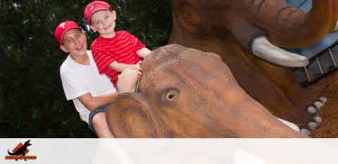 Two smiling children wearing caps sit atop a wooden carving of an elephant.