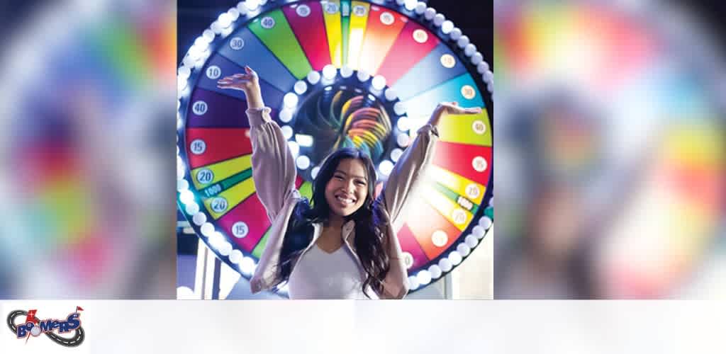 A joyful woman with her arms raised in excitement stands in front of a colorful wheel of fortune game at an arcade.