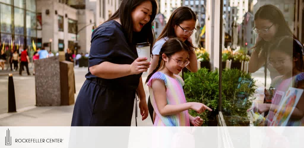 Image Description: Two girls and a woman are peering into a shop window at Rockefeller Center. One girl, wearing glasses, points at something inside, while the other, in a pastel dress, looks on. The woman, holding a beverage, smiles down at them. City life bustles in the background.