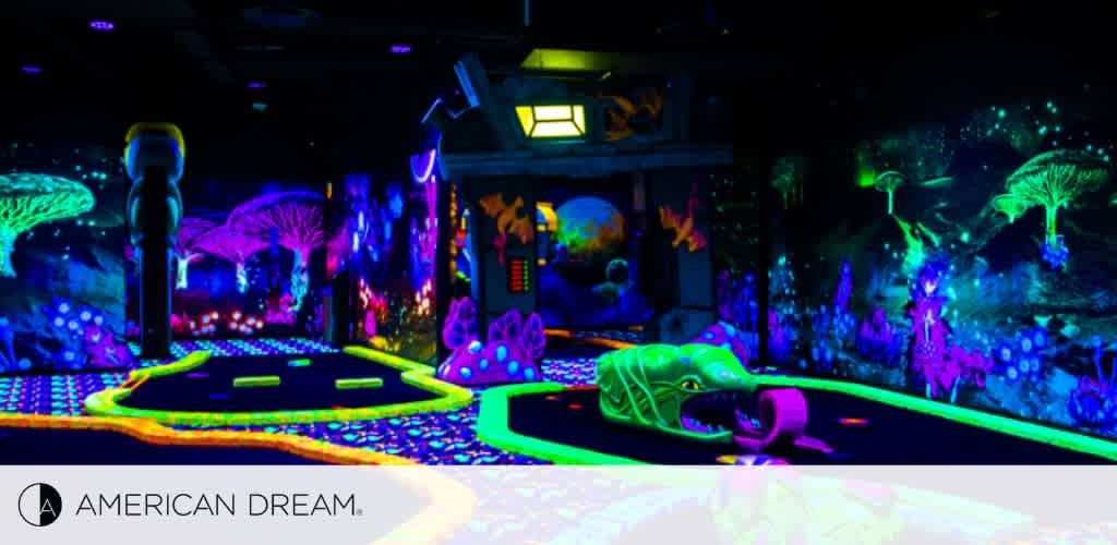 This image showcases a vibrant indoor mini-golf course illuminated by black lights. The neon glow highlights fantastical designs such as mushrooms, sea creatures, and whimsical trees. A playful atmosphere is created by the glowing outlines on the floor and the array of luminous colors. The 'American Dream' logo is visible in the corner, indicating the location.
