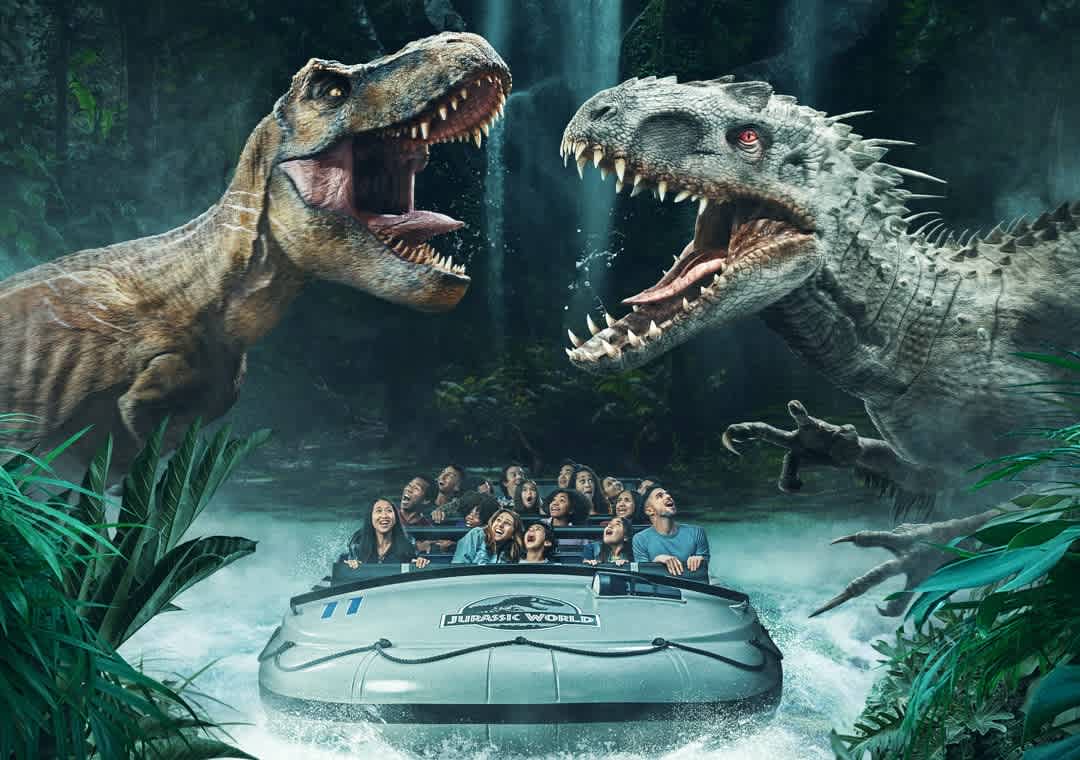 Image shows an animated scene with two large dinosaurs on either side, resembling a T-Rex and another spiky reptile, roaring at a group of excited people in a ride vehicle, amidst a jungle-like setting with misty waterfalls in the background. The individuals appear thrilled by the experience.