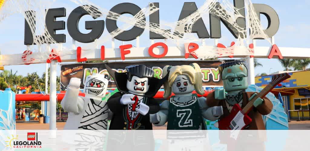 This image displays a welcoming scene at LEGOLAND California with large LEGO letters spelling out the park's name. In the foreground are four life-sized LEGO figure characters dressed in Halloween costumes, including a mummy, vampire, ghost, and Frankenstein's monster, adding a playful, festive atmosphere.