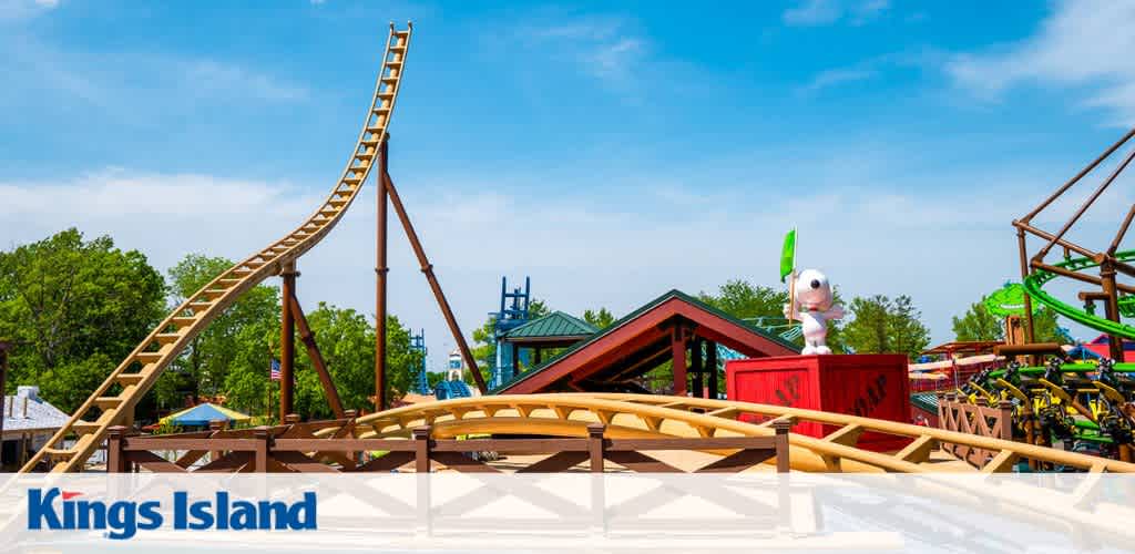 Amusement park scene with a wooden roller coaster and a character statue on a red platform, surrounded by trees and blue sky.