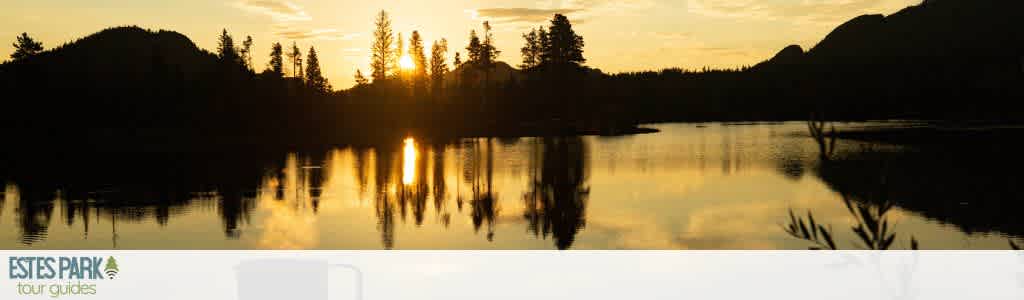 A serene landscape at sunset with a tranquil lake reflecting the golden sky and silhouetted trees. Snow-capped mountains are faintly visible in the distance, creating a peaceful atmosphere. The setting sun casts a warm glow across the scene, offering a calm and picturesque view perfect for nature lovers and adventure seekers.