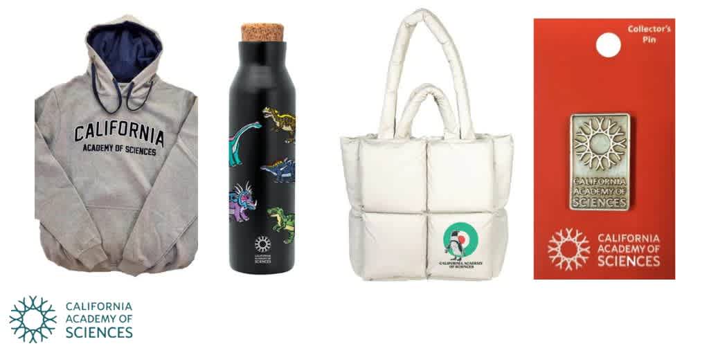 Image showcases merchandise from the California Academy of Sciences: a gray hoodie with the academy's name, a black water bottle featuring colorful dinosaur illustrations, a white quilted tote bag with academy logo, and a collector's pin with the academy's emblem on a red card.