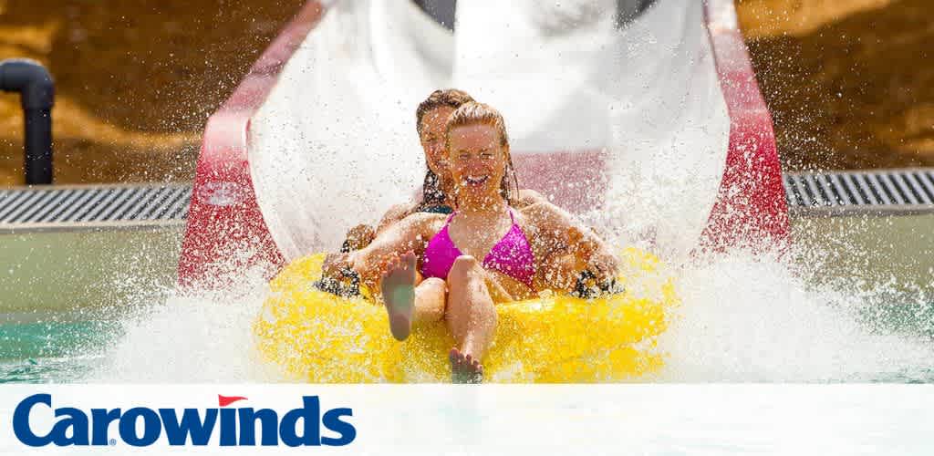 Two people riding a yellow inflatable raft on a water slide, with